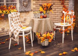 Kolorowe liście rozrzucone na tarasie obok stolika i krzeseł