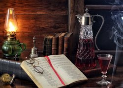 Książki, karafka i lampa naftowa oraz kieliszek z winem w kompozycji