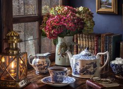 Lampion obok wazonu z kwiatami i zastawy porcelanowej na stole
