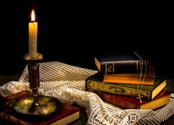 Łańcuszek z krzyżykiem leżący na książkach oświetlonych blaskiem palącej się świecy
