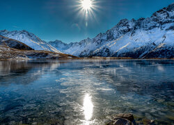 Lód na jeziorze i ośnieżone góry w promieniach słońca