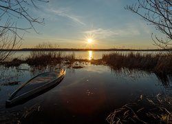 Łódka na brzegu jeziora w promieniach zachodzącego słońca