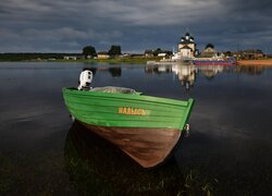 Łódka na jeziorze i cerkiew w oddali pod ciemnymi chmurami