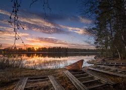Łódka przy brzegu jeziora w brzozowym lesie o zachodzie słońca