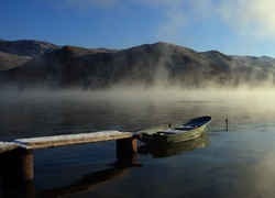 Łódka przycumowana do pomostu na zamglonym jeziorze w górach
