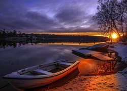 Łódki nad brzegiem jeziora w blasku słońca zachodzącego za drzewa