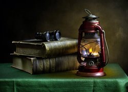 Lornetka na książkach obok lampy naftowej