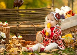 Mała dziewczynka z kukurydzą wśród jesiennych liści i warzyw