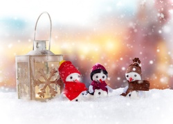 Małe bałwanki w ubrankach z lampionem na śniegu