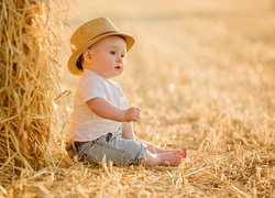 Mały chłopczyk siedzi obok beli siana