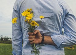 Mężczyzna z polnymi kwiatami w ręce za plecami