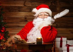 Mikołaj z piórem i listem obok choinki i prezentów