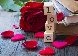 Napis Love ułożony z klocków obok książek i róży