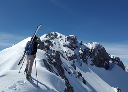 Narciarz idący po zaśnieżonym szczycie góry