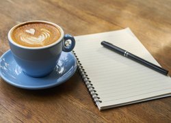 Niebieska filiżanka z kawą obok długopisu na notesie