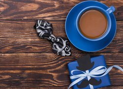 Niebieski prezent i filiżanka kawy dla taty obok muszki na deskach