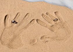 Odcisk dłoni z obrączkami na piasku