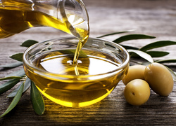 Olej w miseczce obok oliwek na deskach