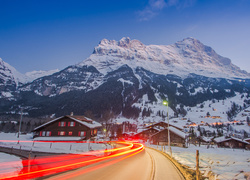 Oświetlona droga prowadząca do zaśnieżonej wioski w górach