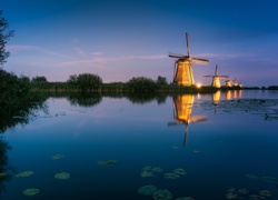 Oświetlone wiatraki nad rzeką w holenderskiej wsi Kinderdijk o świcie