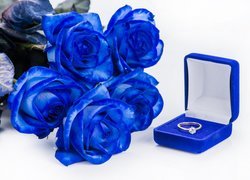 Pierścionek zaręczynowy w pudełku obok niebieskich róż