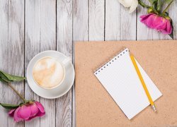 Piwonie obok kawy i notesu z ołówkiem na desce