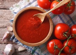 Pomidory na gałązce obok miseczki z sosem pomidorowym