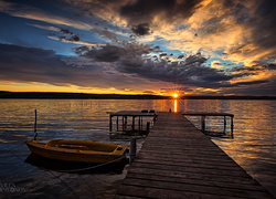 Przycumowa łódka przy pomoście nad jeziorem o zachodzie słońca