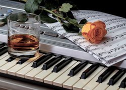 Róża i nuty położone obok szklanki na keyboardzie