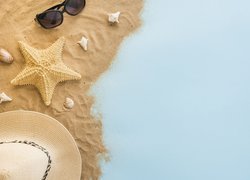 Rozgwiazda z muszelkami obok kapelusza i okularów na piasku