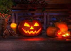 Rozświetlona dynia obok szyszek i i świecy w kompozycji na Halloween
