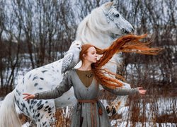 Rudowłosa kobieta z sową na ramieniu obok konia