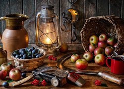 Śliwki i jabłka w koszyku obok lampy i dzbanka