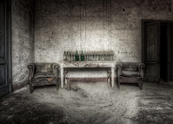 Stare fotele obok stołu zastawionego pustymi butelkami
