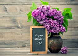 Tabliczka z życzeniami na Dzień Matki oparta o wazon z kwiatami bzu