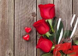 Trzy czerwone róże i kieliszki obok serduszek na deskach