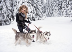 Uśmiechnięta blondynka z psami siberian husky na spacerze w zaśnieżonym lesie