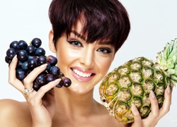 Uśmiechnięta kobieta z ananasem i winogronami w dłoniach