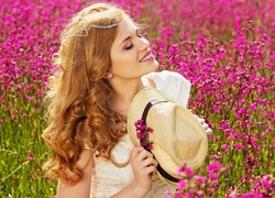 Uśmiechnięta kobieta z kapeluszem w dłoniach na wiosennej łące