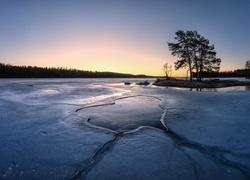 Wysepka z drzewami na jeziorze skutym lodem z widokiem na zachód słońca