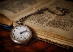 Zegarek kieszonkowy z łańcuszkiem położony obok książki