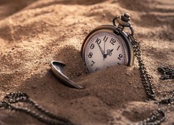 Zegarek na łańcuszku przysypany piaskiem