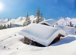 Zimowy górski krajobraz z zaśnieżonymi drewnianymi chatami w słońcu
