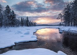 Zimowy wschód słońca nad zaśnieżoną rzeką i lasem