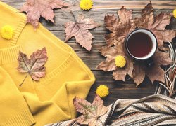 Żółty sweter obok kubka kawy na liściach