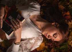 Kobieta z książką leżąca na liściach