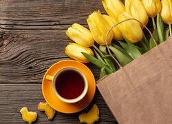 Żółte tulipany w papierowej torbie obok filiżanki z kawą