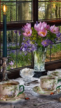 Bukiet kwiatów obok świecy i serwisu do kawy