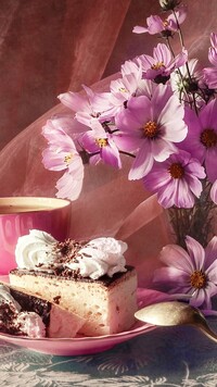 Kawałek ciasta obok różowej kosmei w wazonie