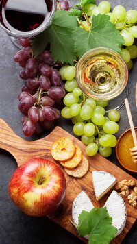 Kieliszki z winem obok winogron i deski z serem
